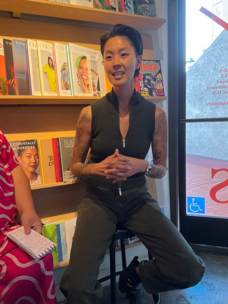 Chef and host of Top Chef Kristen Kish speaking at Now Serving LA bookstore in Chinatown, Los Angeles, about her memoir Accidentally on Purpose. Kidh is Korean-American, 5’9” tall, wearing dark pants and a sleeveless top. Both arms are tattooed in drawings, including a canoe commemorating a trip in Calgary that will air later this season on Top Chef. Photograph by M.C. Valada, 2025.