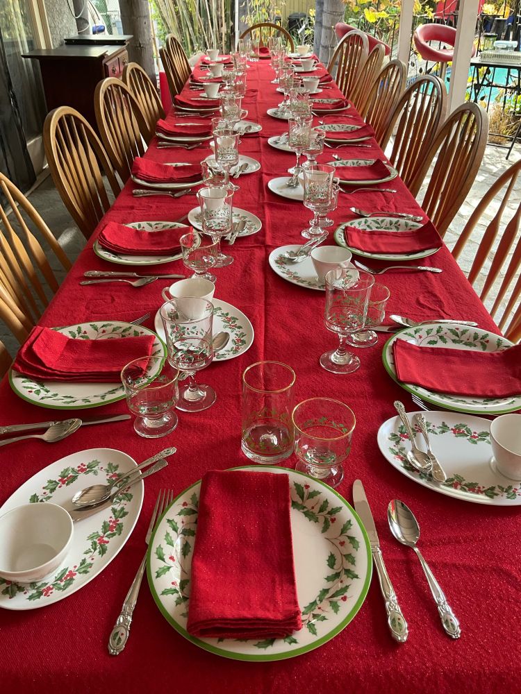 Christmas table setting featuring Lenox Holiday plates and flatware of holly and berries on a red table cloth with red napkins. Collectible Arby Christmas stemmed glassware.