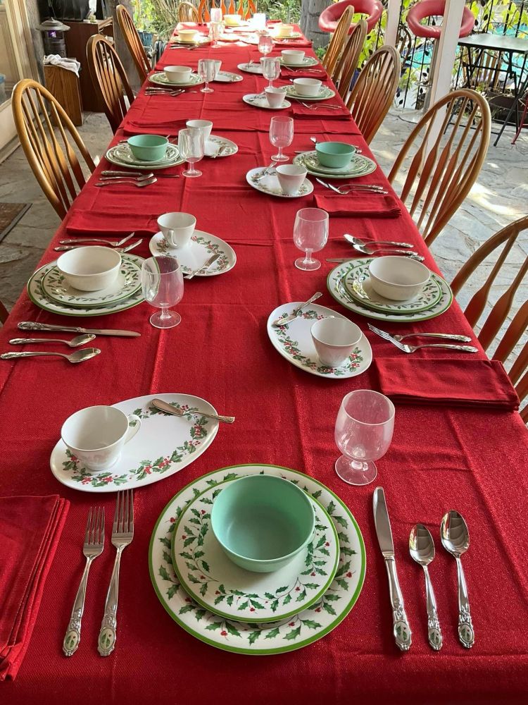 Outdoor on the veranda table-setting for 10 at Christmas Tea, using Lenox Holiday melamine dishes (holly and berry design) and Lenox stainless Holiday flatware. Tea cups are on mid-century oval tea-and-toast/snack plates which match the Holiday pattern. Red with metallic gold table cloth and napkins, plain stemmed acrylic water glasses. 