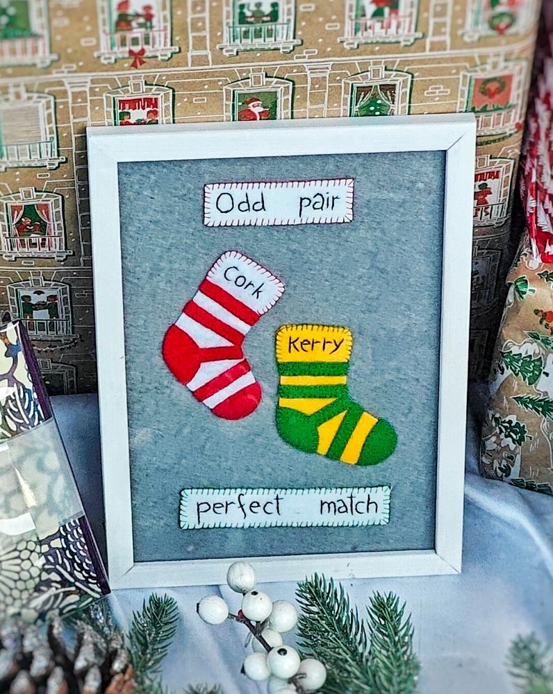 Photograph of a handmade piece in a frame in a shop window, showing two socks in Cork and Kerry colours, labelled "Odd Pair", "Perfect Match". Kerrypeople, be on your guard.

#SpéirGhorm #SpéirGorm