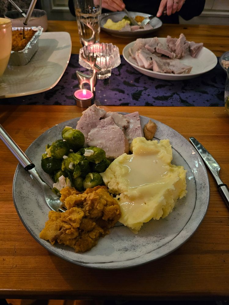 A plate of Thanksgiving food on a table. Swede, mashed potatoes, honey and maple sprouts, and ham. 