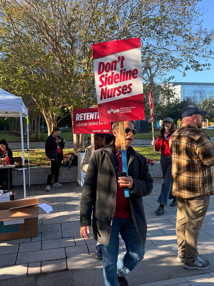 Striking nurse at University Medical Center New Orleans carrying a sign that reads "Don't sideline nurses"