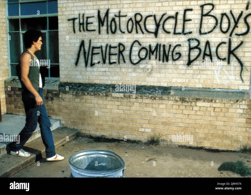 Bilde fra filmen Rumble Fish som viser en ung mann foran en vegg med grafitti som sier The Motorcycle Boy's Never Coming Back.