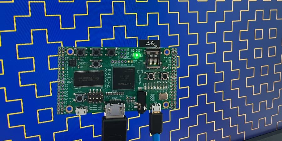 ULX3S FPGA dev board connected to LCD monitor showing hitomezashi stitch pattern in bright yellow on a blue background.