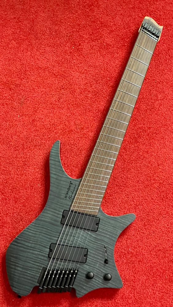 Dark grey strandberg headless 8-string guitar on red carpet. 