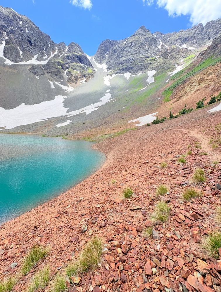 A high altitude lake with turquoise color water against the base of the peaks making up the basin.