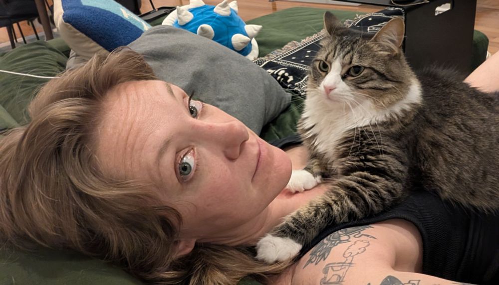 Me lying on my couch with my cat Doug on my chest, essentially hugging my neck