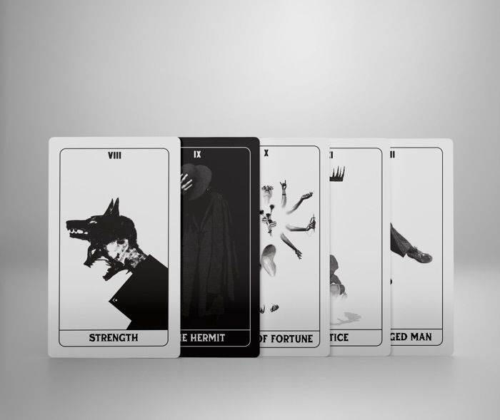 5 monochrome tarot cards are lined up in a row, some obscuring others. The first one is strength showing artwork with a man with two dog faces screaming. The other artwork is obscured but the words “hermit” “fortune” and “man” can be made out on the other cards. The card tucked behind the first is black with white accents and all others are white with black accents. 