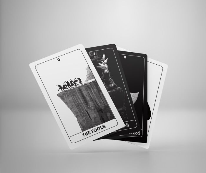 Four monochrome cards are spread out like a fan, most of the artwork is obscured in a stylish manner, but the first card is completely visible. It has “The fools” printed on the bottom and depicts a group of dancers dancing precariously near a cliff. 