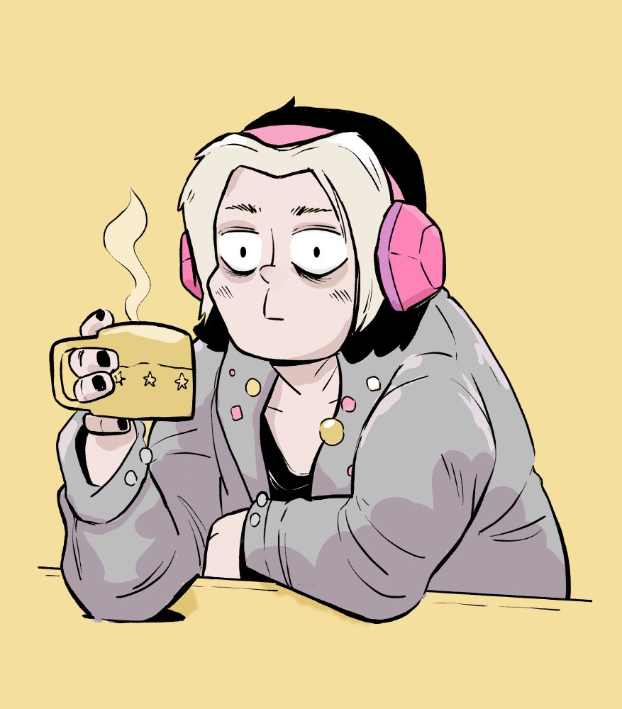 a man leaning again a table drinking coffee. he has pink headphones on and is wearing a long gray coat.