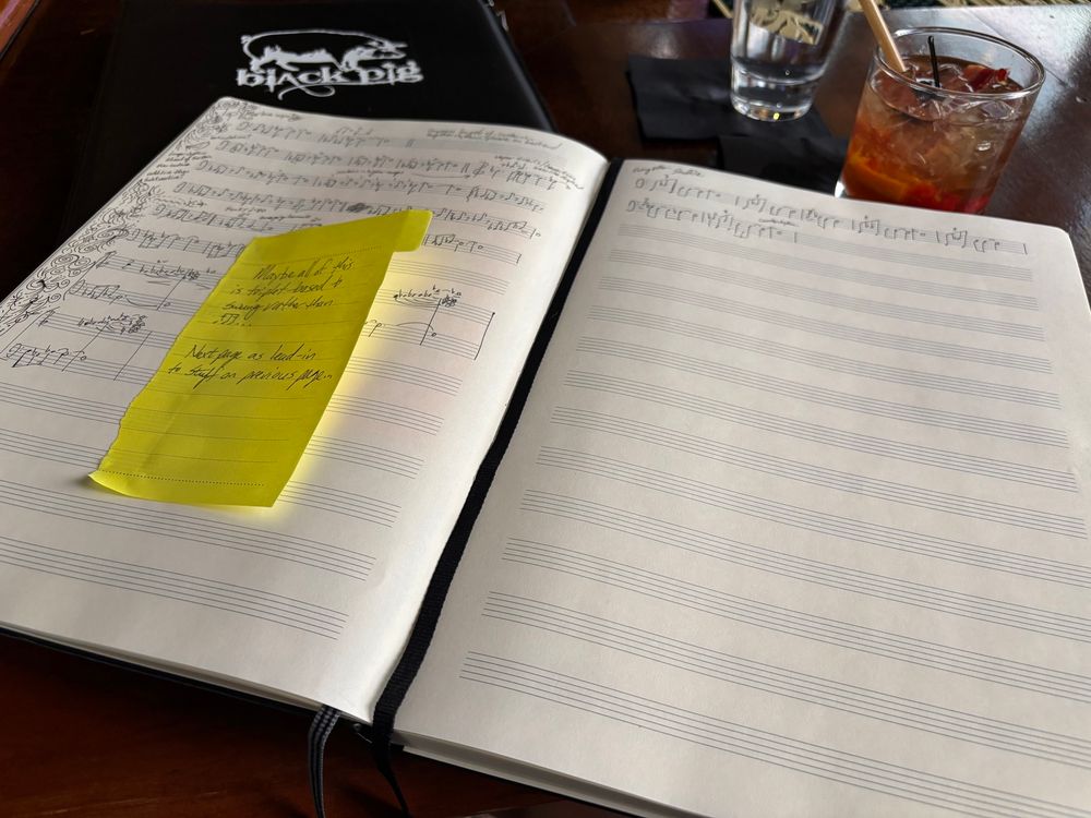 A music manuscript notebook lies open on a bar. In the upper right corner, there’s a cocktail…an old fashioned. It’s garnished with bacon because why the hell not?