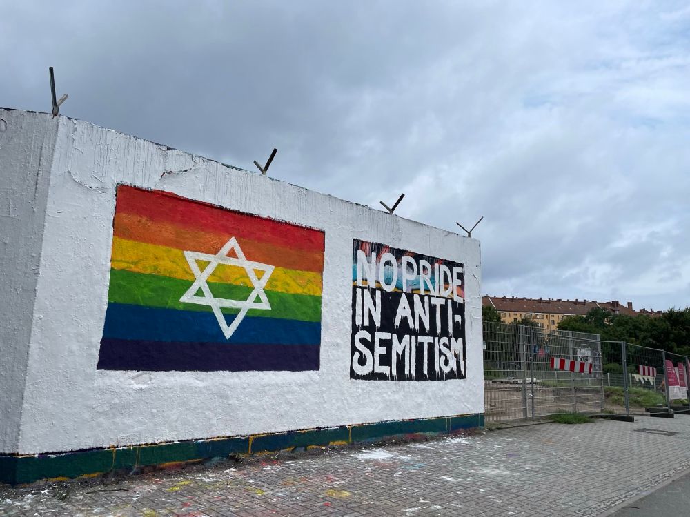 Wand am Tempelhofer Feld, darauf eine Regenbogenfahne mit Davidstern, daneben steht: No Pride in Antisemitism. 