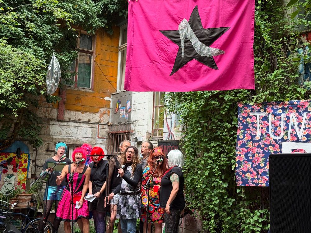 Der Rattenchor im Tuntenhaus, darüber die pinke Fahne mit dem Stöckelschuh auf dem schwarzen Stern.