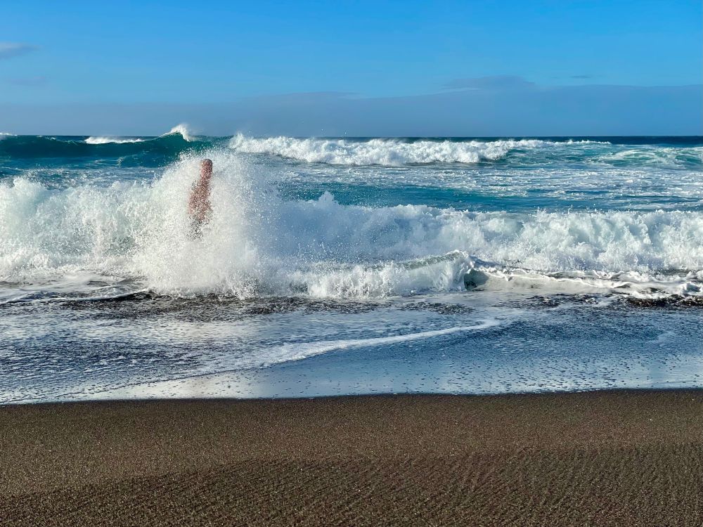 Blick auf das Meer, viele WQellen, links ist eine Person in den Wellen kaum zu erkennen.