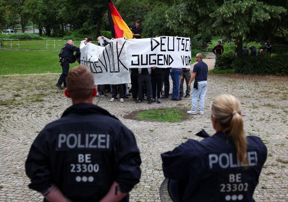 Im Vorderund Cops, dahinter die Nazis eingewickelt in ihren Fahnen auf engen Raum.