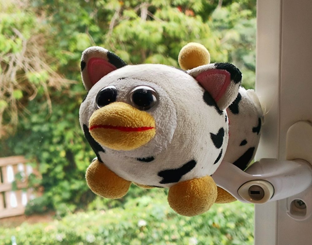 peepy propped on a window handle, with blurred greenery behind him. he sports a wide-eyed slight grin, with strangely hollow eyes