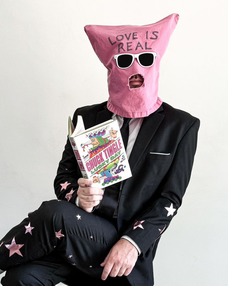 chuck tingle lookin DANG HANDSOME with a suit covered in stars holding lucky day (the worlds greatest book)
