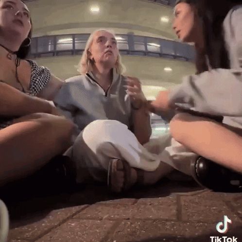 a group of women are sitting on the ground and one of them has tiktok written on the bottom