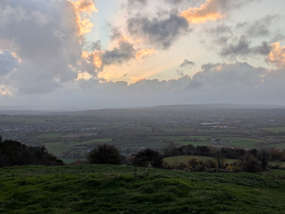 The sun cutting through the clouds over a wide, green valley