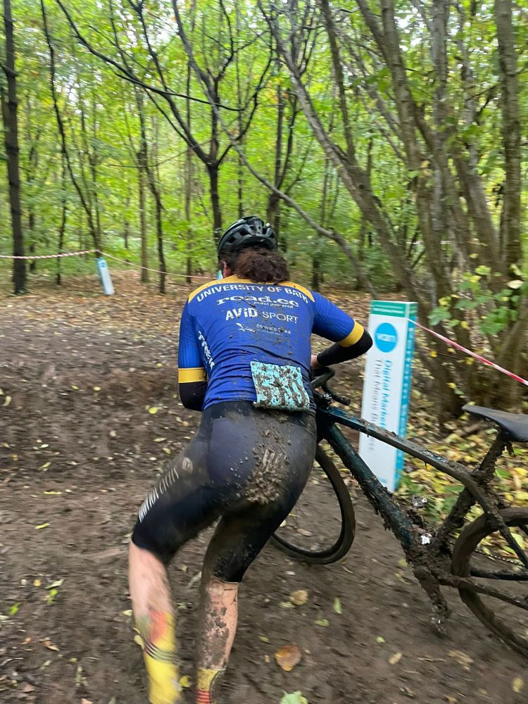Me in a blue and yellow jersey running with my muddy bike towards a muddy ditch 