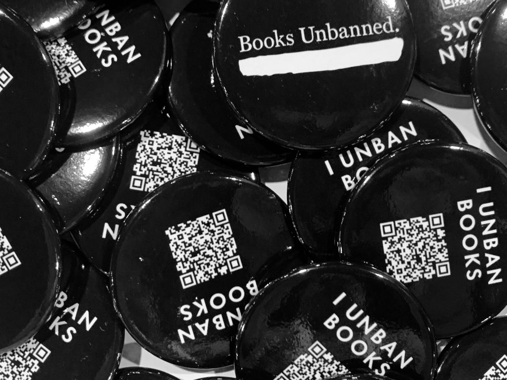 Picture of black and white buttons. They say “I unban books,” with a QR code. 