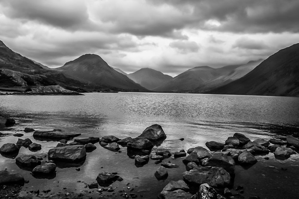 Rocks in the foreground at the edge of Wastwater, looking towards, Yewbarrow, Great Gable, Lingmell and the side of Scafell Pike. Taken in black and white on a cloudy day.