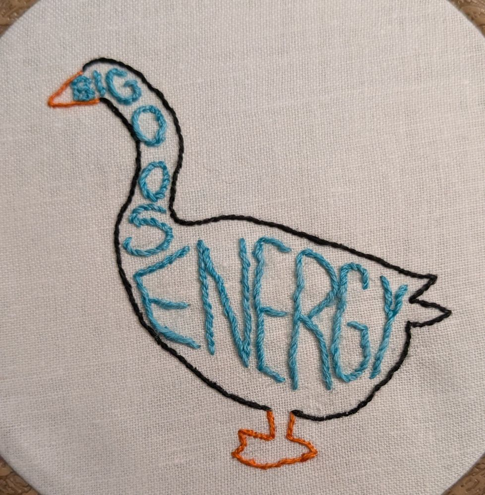 Photo of an embroidered outline of a goose in black thread with orange beak and feet. Inside the outline fitted to the shape of the goose says "big goose energy"