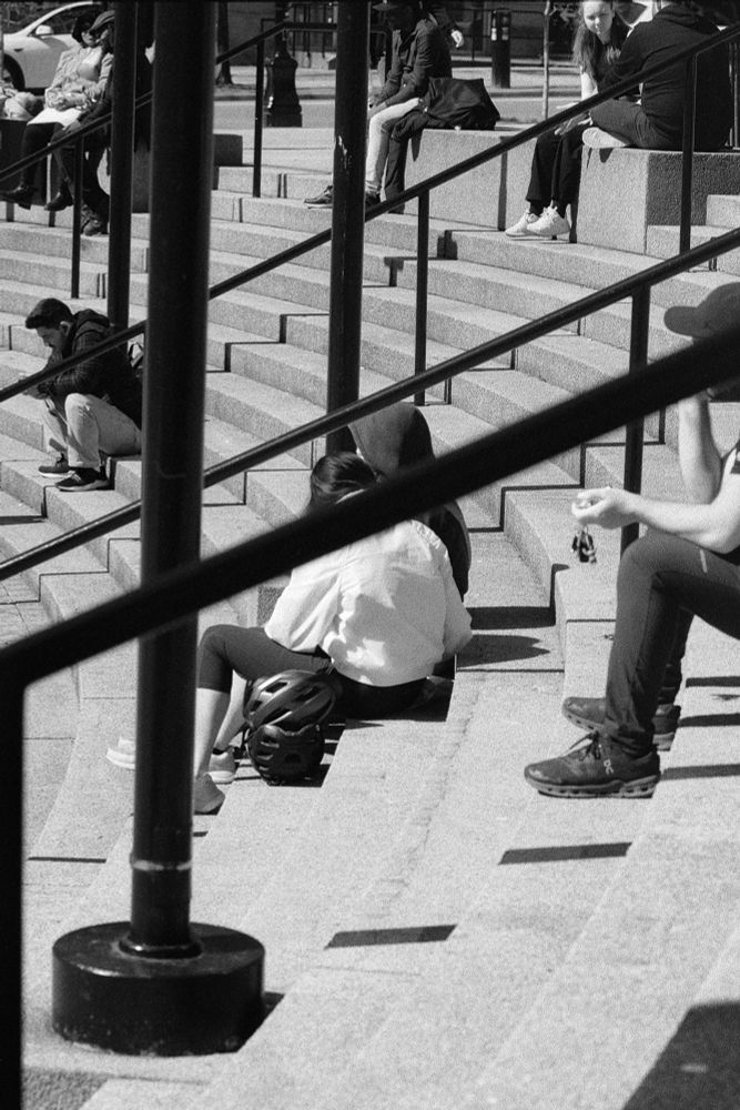 People sit in the warm sunlight on the curved steps approaching a building.