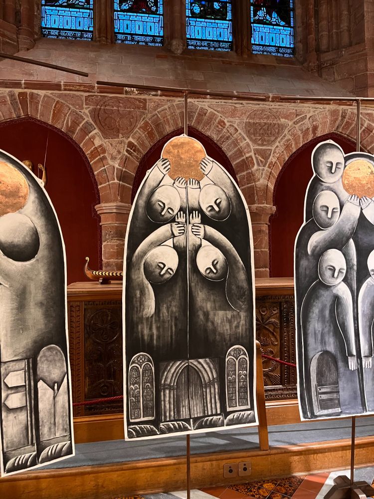 Large monoprints featuring stylised figures holding golden balls. Church architecture in the background.