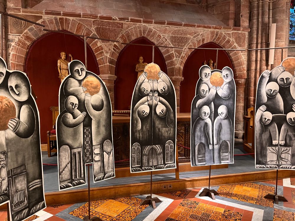 Large monoprints featuring stylised figures holding golden balls. Church architecture in the background.