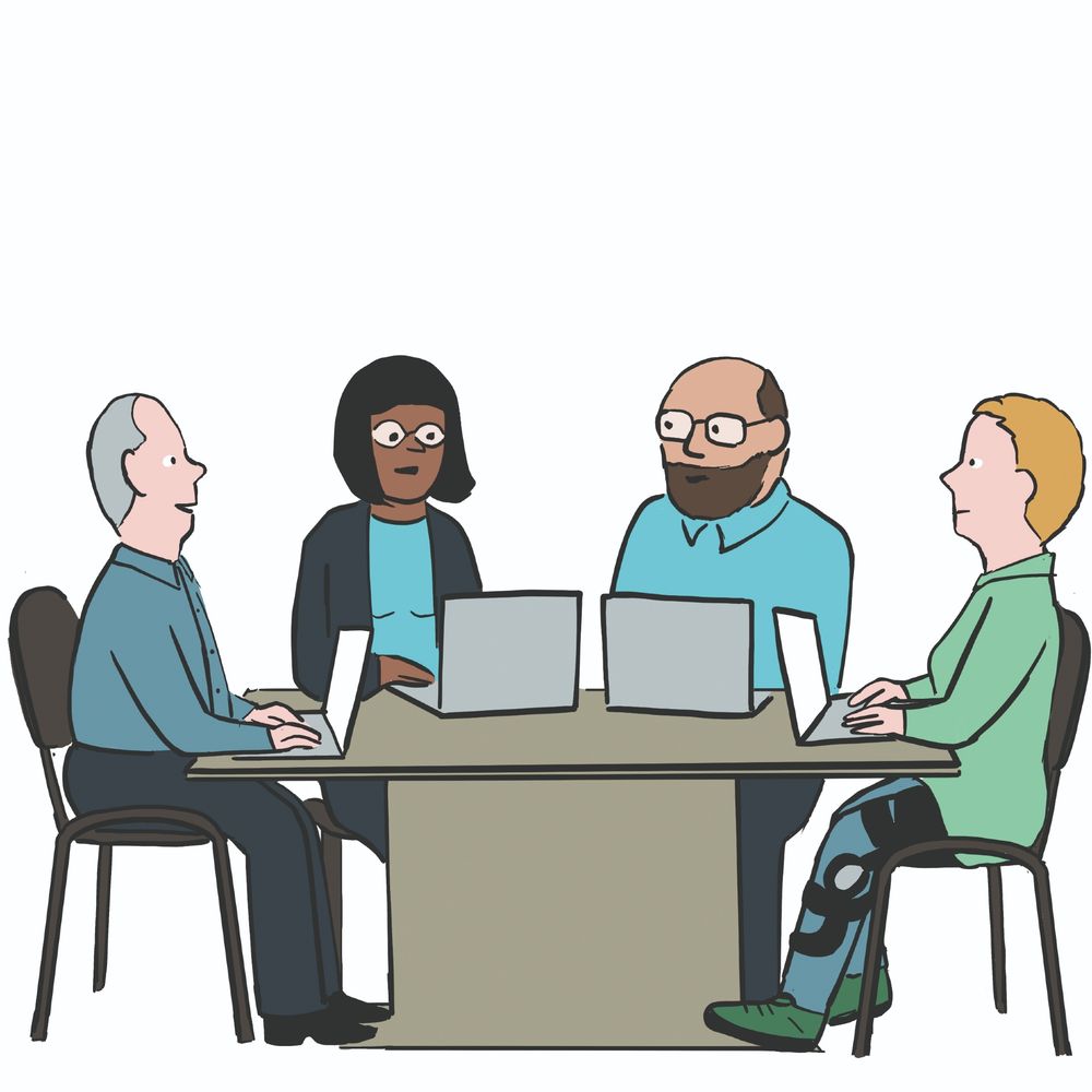 Vier Menschen sitzen an einem Tisch. Vor ihnen auf dem Tisch stehen Laptops. Sie unterhalten sich.