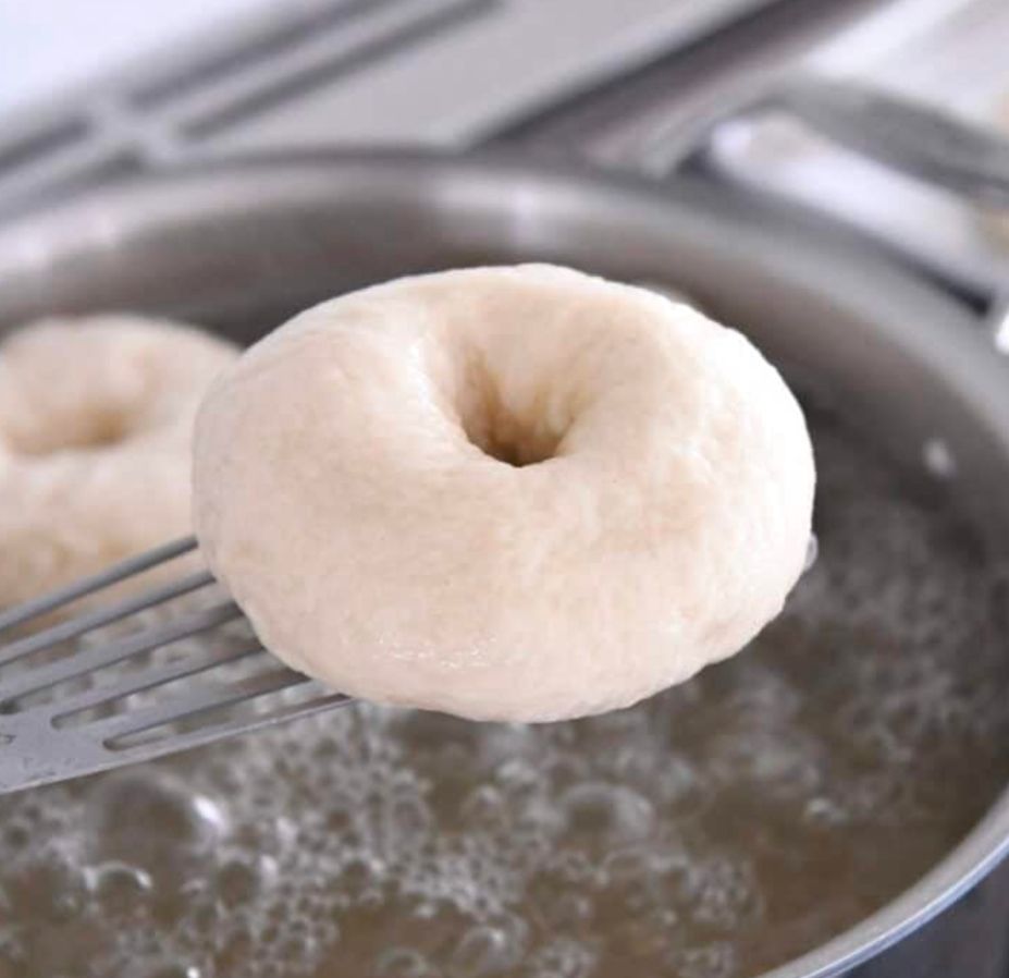 A picture of a raw bagel about to be boiled. Boiling the dough gives the bagel a superior texture to baking alone 