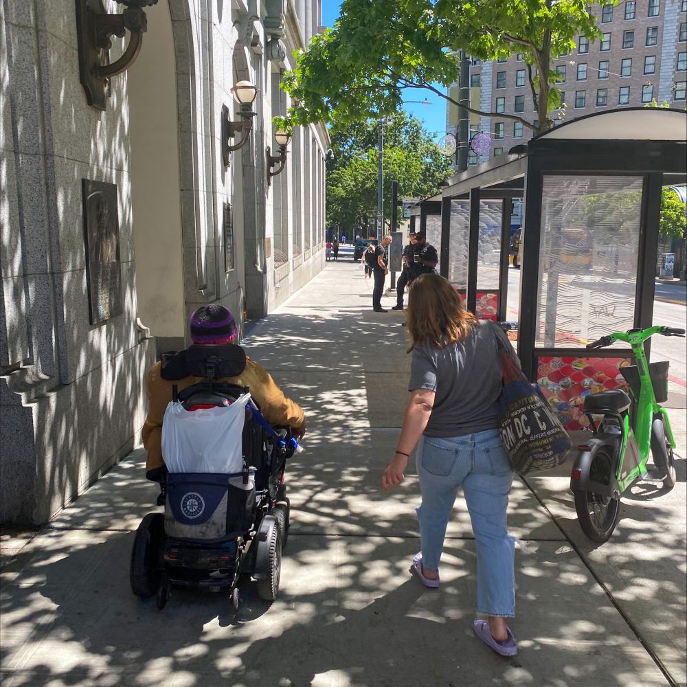 People walk and roll along 3rd Ave in downtown Seattle near bus stops.