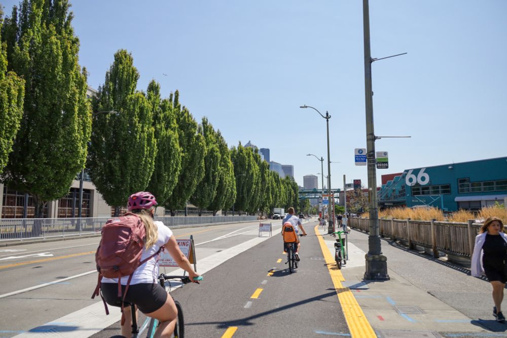 A person carrying a child and another person ride in the protected bike lanes along Alaskan Way, near Pier 66.