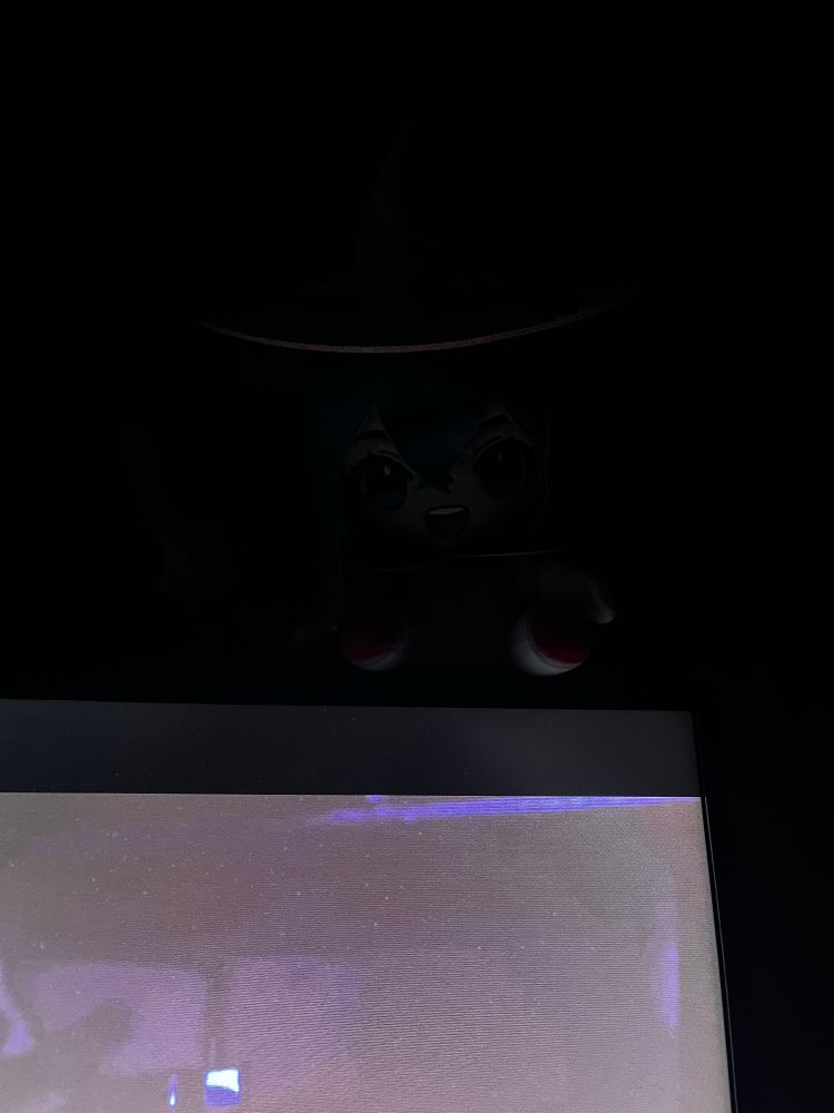 A Racing Miku plush sitting on top of a lit monitor in a dark room