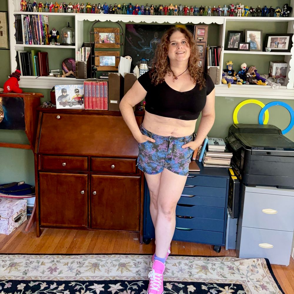 Jadzia is wearing a heart-shaped carnelian necklace, a cropped black t-shirt, high-waisted shorts with a galaxy pattern, purple socks and pink Converse sneakers.