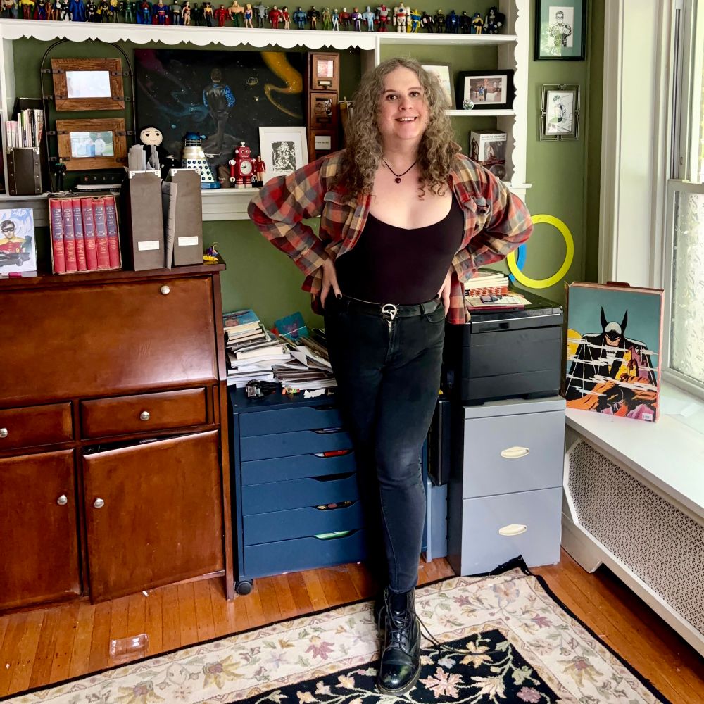 Jadzia is wearing a necklace with a small carnelian heart-shaped pendant, a red and gold flannel shirt over a black tank top, black high-waisted skinny jeans, and black Doc Marten boots.