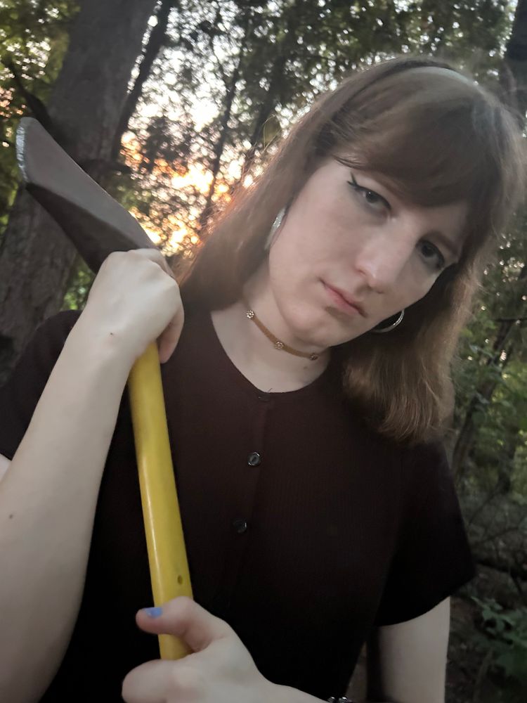 Taylor in a dress in the woods with an axe 