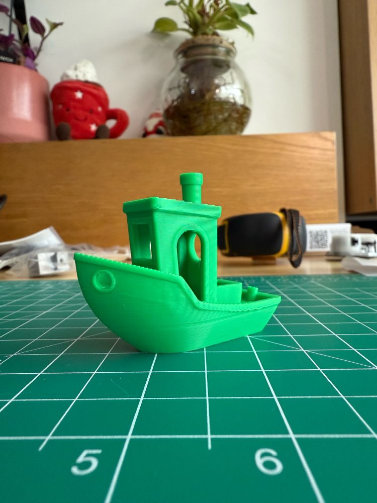 A “benchy” 3D printing benchmarking boat model in green PLA sitting on a cutting board.