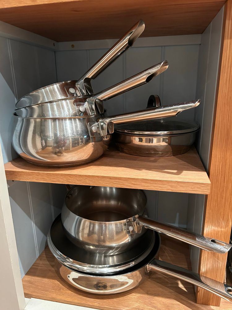 A stack of stainless steel saucepans on oak shelving.