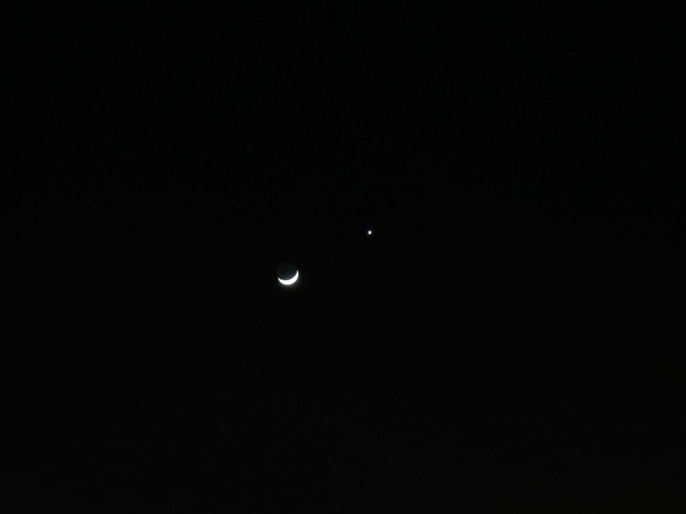 The waxing crescent moon is flanked by a star, the planet Venus.