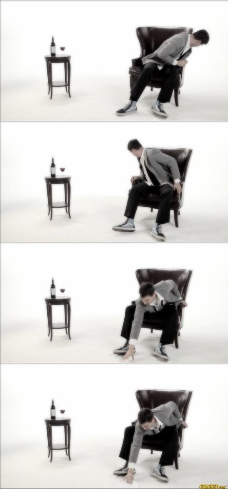 A man sits in a wing-back chair next to a decorative little table with a bottle of wine and a glass on it, in an otherwise featureless white room. He looks down and to his left, right, and behind him. Finally he bends forward and gropes at a spot on the floor between his feet, and picks up the white sheet of paper he’d dropped.