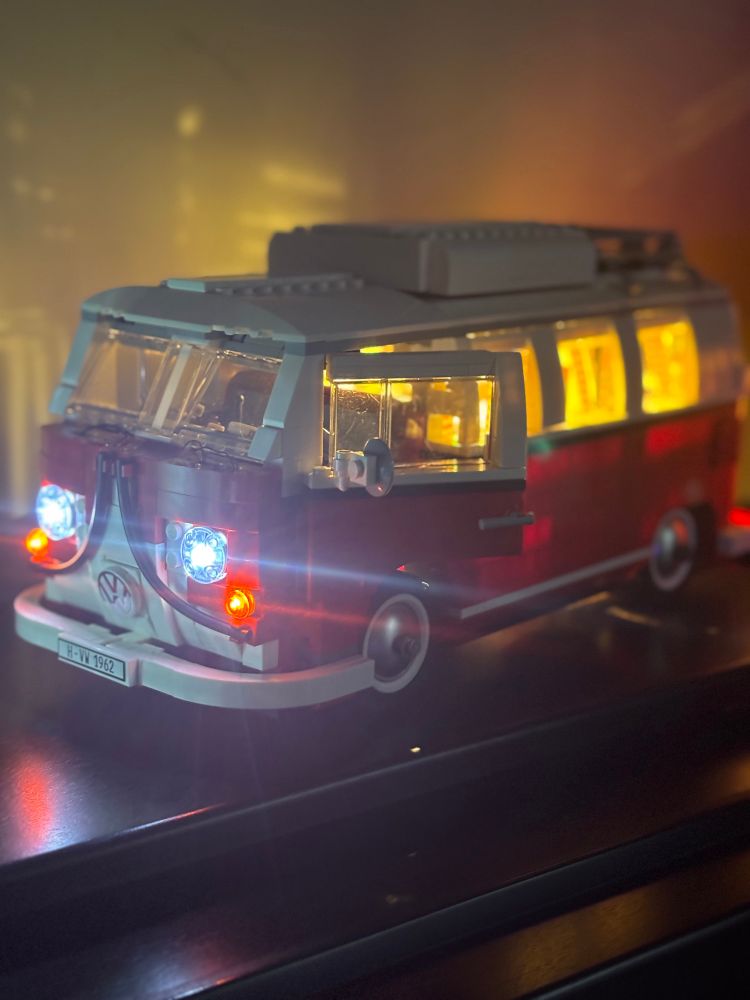 A classic red VW campervan built from LEGO, with glowing headlights and interior lights.
