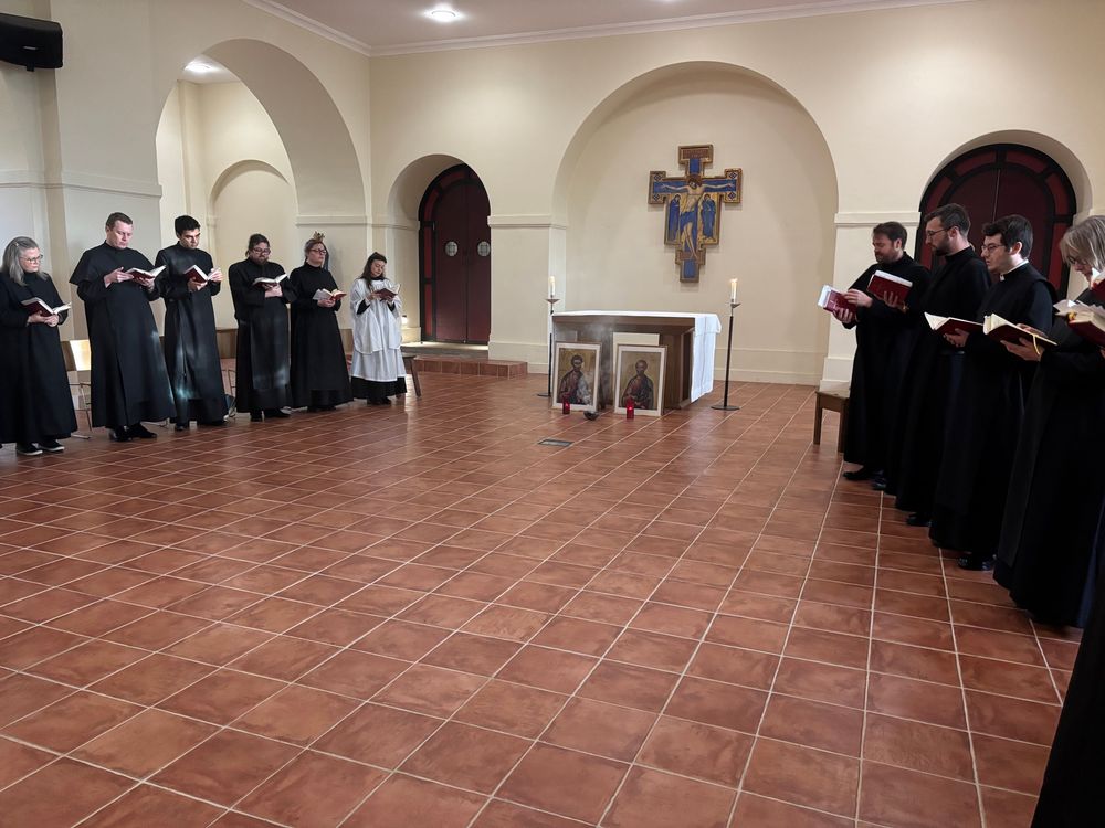 A group of people in cassocks praying in a chapel. Two large icons are placed in front of the altar and a bowl of incense is being burned.