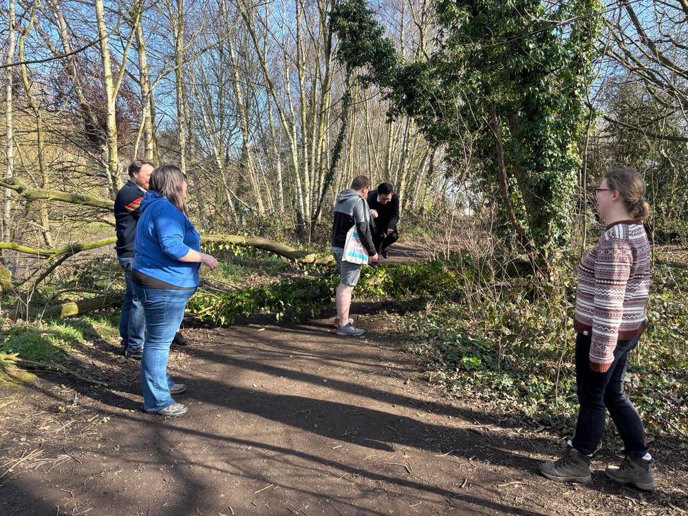 A group of men and women on a path through the woods. It is a fine day in early spring.