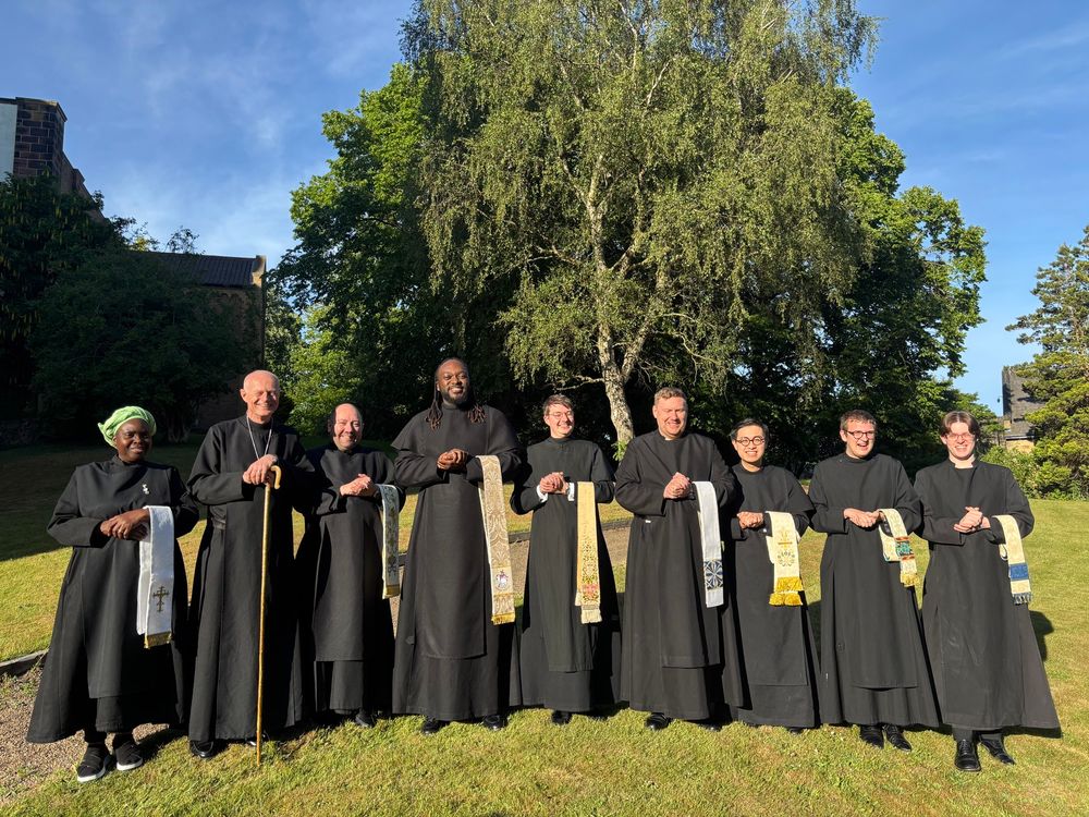 A group of men and women in cassocks with stoles over their arms.