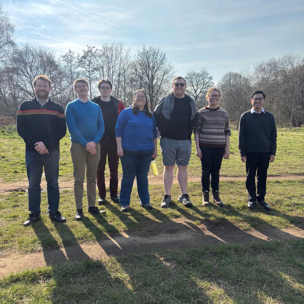 A group of men and women on a grassy path, smiling at the camera.
