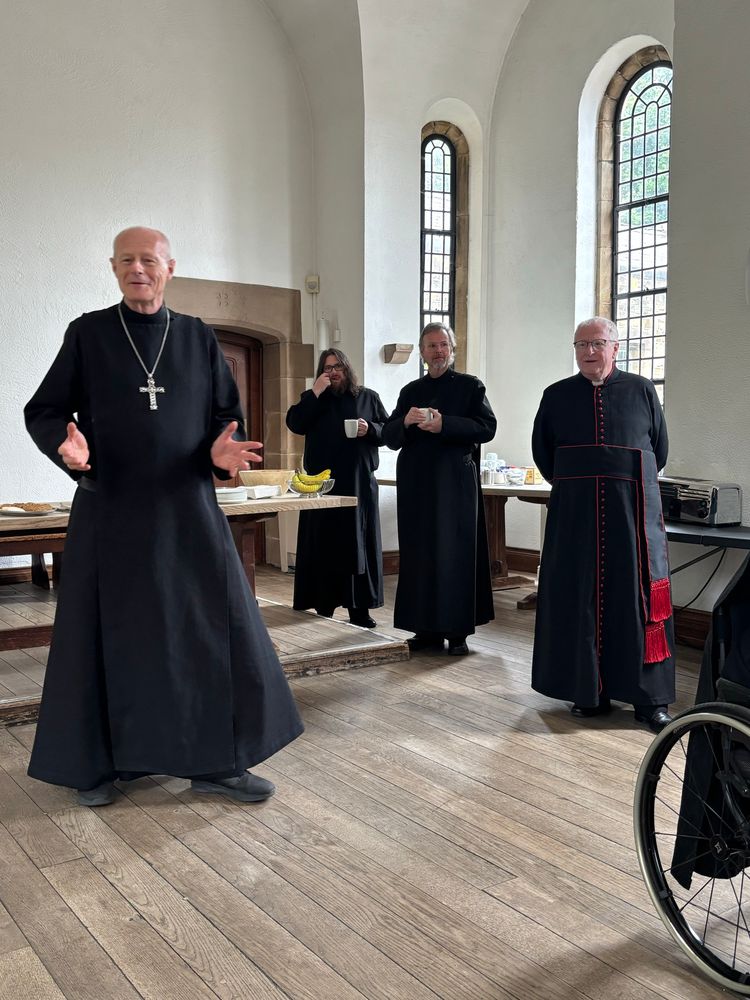 Several men in cassocks. One, who is talking, is a bishop.