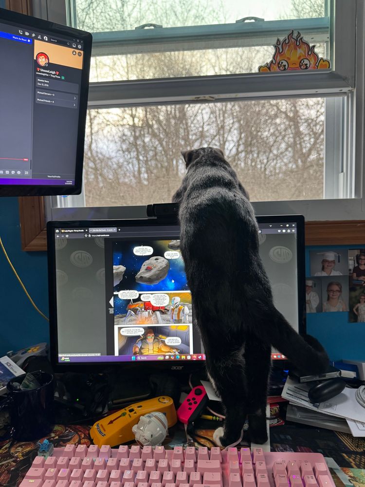 A black cat with white paws in front of a pink keyboard leaning of a computer monitor with a comic on it, to look out of an open window. 