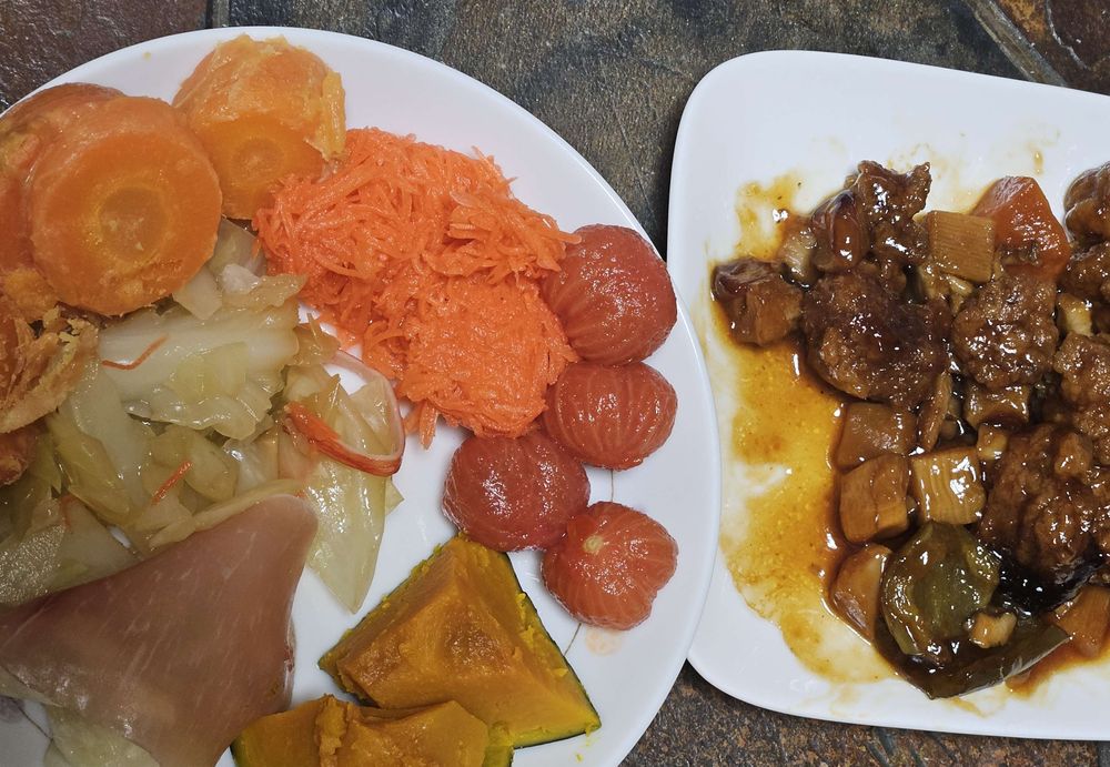 1つ目の皿。蒸しキャベツ、トマトピクルス、甘酢人参、皮付人参のグラッセ、万能塩蒸しかぼちゃ。2つ目の皿、レトルトやわらか酢豚。全体的に暖色のおかずが集まっています。